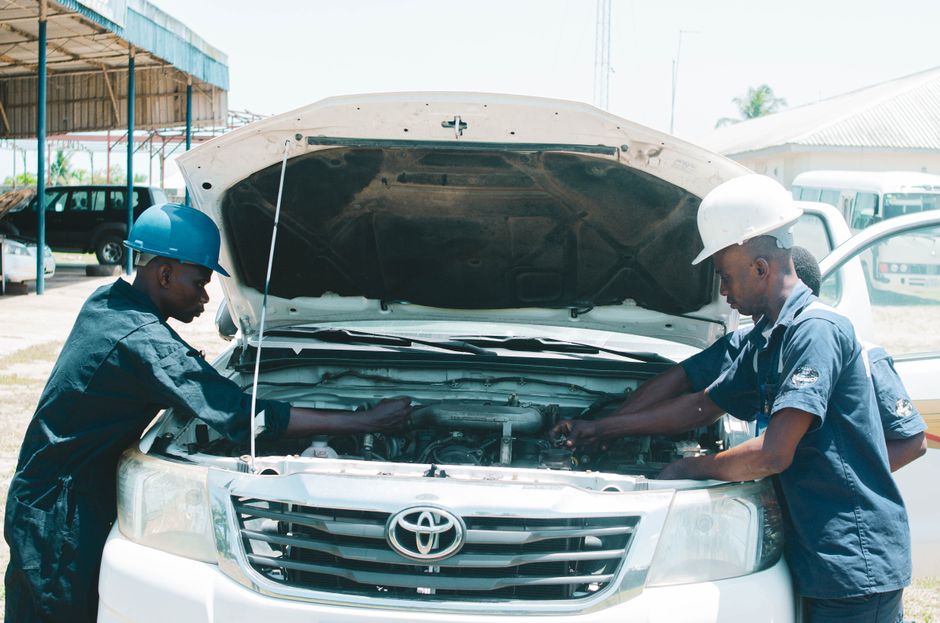 Two African mechanics checking a Toyota engine outdoors in AK, Nigeria, showcasing teamwork and collaboration.